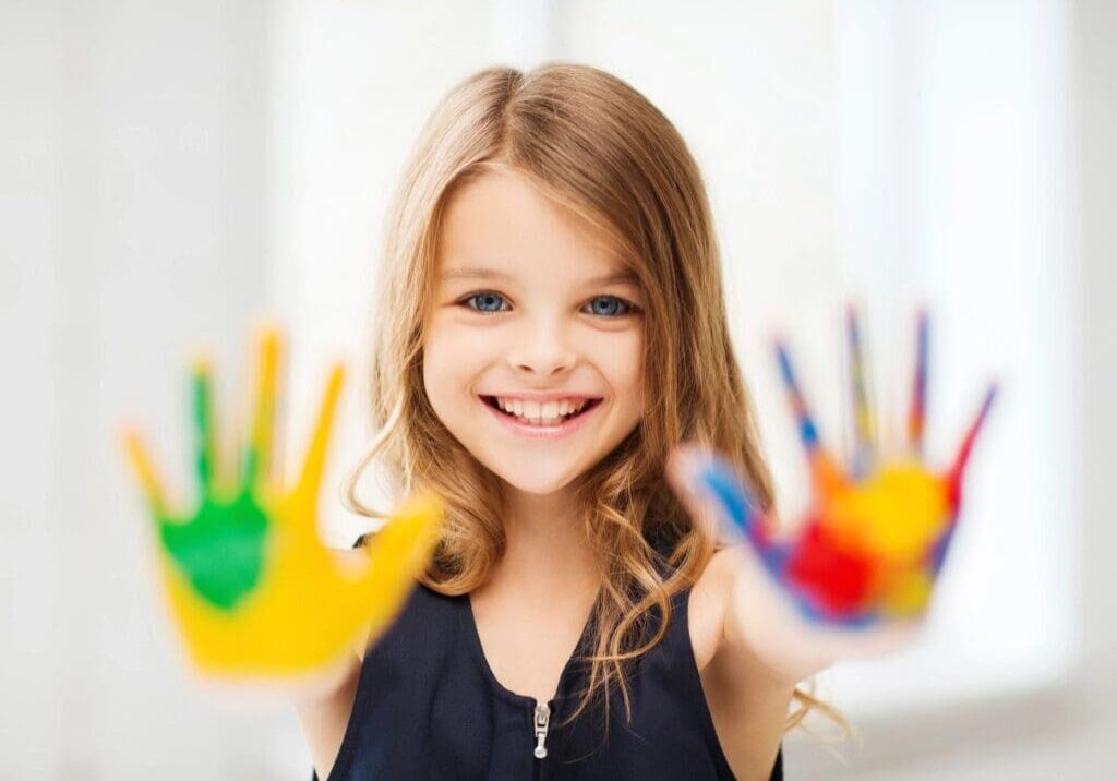 A little girl with her hands painted in different colors.